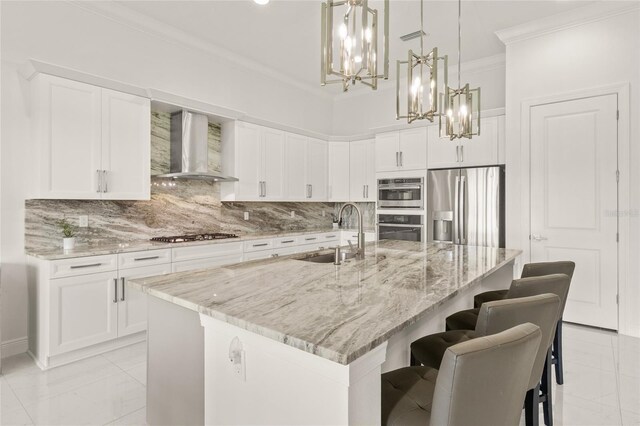 kitchen featuring wall chimney range hood, a sink, stainless steel appliances, crown molding, and a chandelier