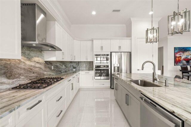 kitchen with wall chimney exhaust hood, a sink, appliances with stainless steel finishes, crown molding, and a chandelier