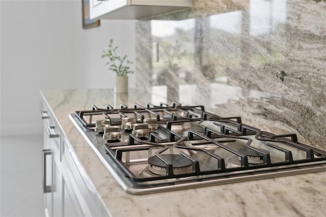 detailed view of stainless steel gas stovetop, white cabinetry, and light stone countertops