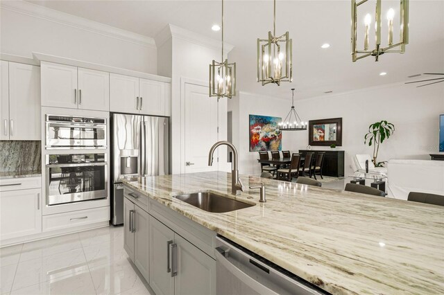 kitchen with a sink, a chandelier, crown molding, appliances with stainless steel finishes, and light stone counters