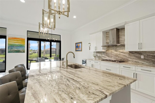 kitchen featuring wall chimney exhaust hood, a chandelier, a sink, stainless steel gas stovetop, and light stone countertops