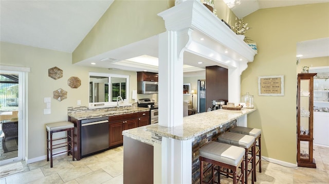 kitchen with a kitchen bar, light stone countertops, a sink, a peninsula, and stainless steel appliances