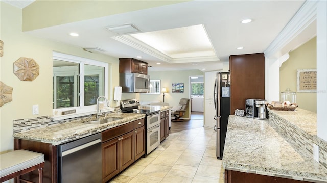 kitchen with washer and dryer, a tray ceiling, light stone counters, a sink, and stainless steel appliances