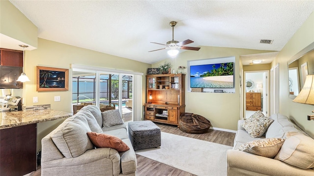 living room featuring wood finished floors, a ceiling fan, lofted ceiling, and visible vents