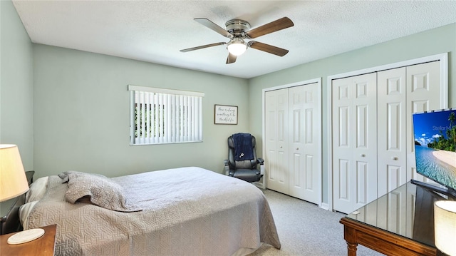 carpeted bedroom featuring a textured ceiling, ceiling fan, and multiple closets