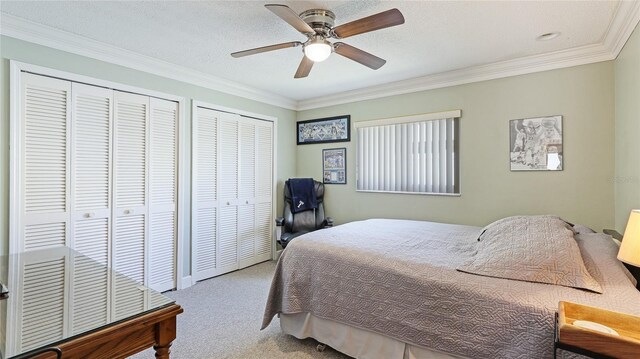 bedroom with crown molding, a ceiling fan, carpet, and two closets