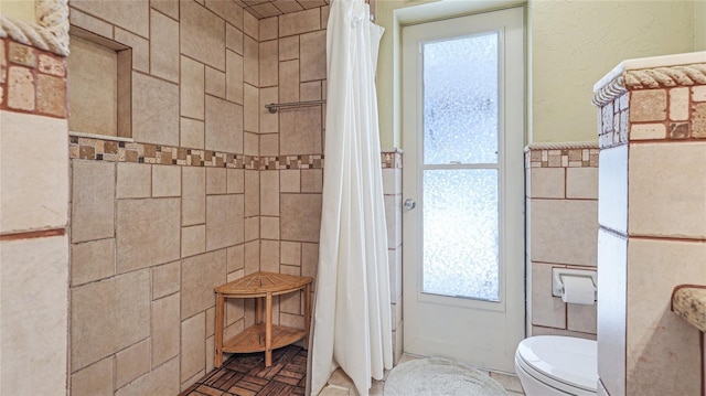full bath with toilet, tile walls, a tile shower, and a healthy amount of sunlight