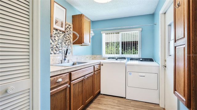 laundry area with washing machine and dryer, light wood-type flooring, a textured ceiling, a sink, and cabinet space