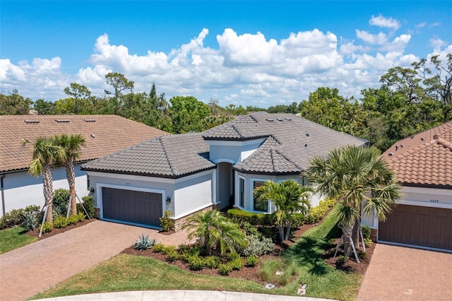 mediterranean / spanish-style home with a tiled roof, an attached garage, decorative driveway, and stucco siding