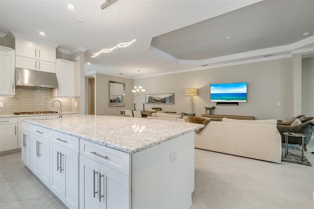 kitchen featuring under cabinet range hood, tasteful backsplash, open floor plan, ornamental molding, and light tile patterned floors