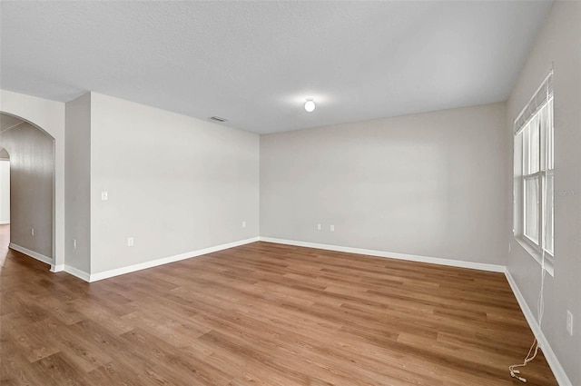empty room with wood finished floors, a textured ceiling, baseboards, visible vents, and arched walkways