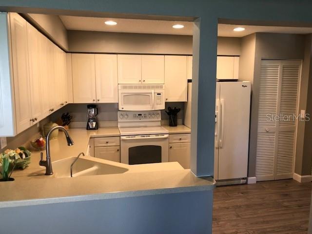 kitchen with dark wood-style flooring, white cabinetry, a sink, recessed lighting, and white appliances