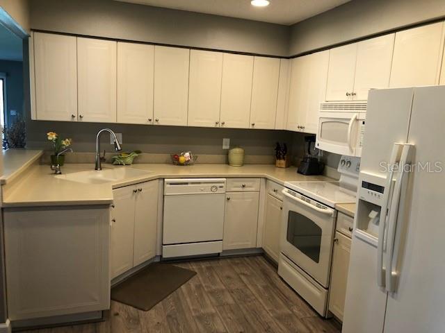 kitchen with white appliances, white cabinets, a sink, and dark wood-type flooring