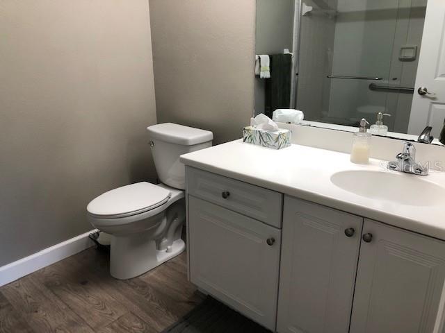 bathroom with a stall shower, wood finished floors, vanity, baseboards, and toilet
