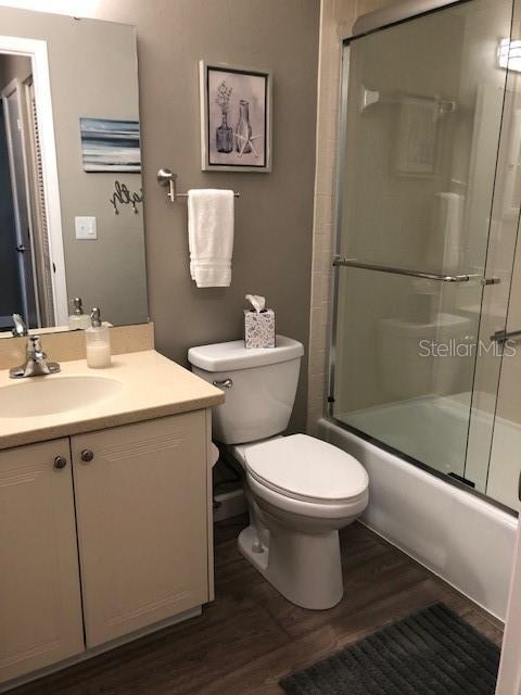 full bathroom with toilet, wood finished floors, bath / shower combo with glass door, and vanity