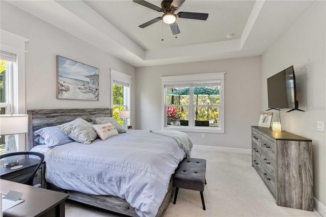 bedroom featuring multiple windows, light colored carpet, a tray ceiling, and baseboards