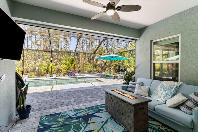 view of patio / terrace with a lanai, ceiling fan, an outdoor living space with a fire pit, and a pool with connected hot tub