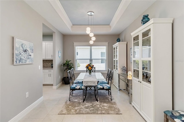 dining room featuring light tile patterned floors, a tray ceiling, baseboards, and crown molding