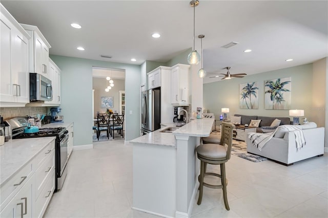 kitchen featuring stainless steel appliances, a sink, backsplash, a kitchen bar, and white cabinetry
