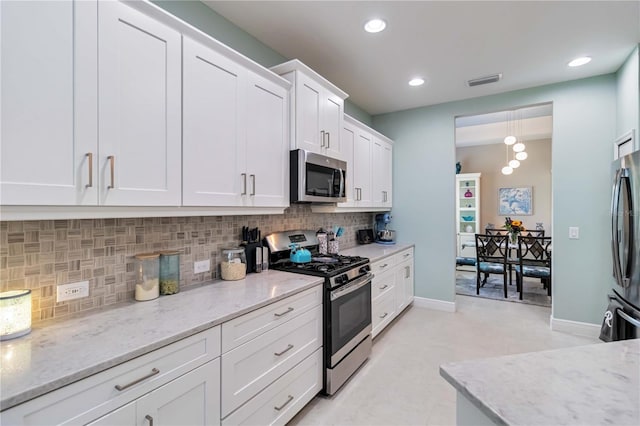 kitchen featuring stainless steel appliances, white cabinetry, tasteful backsplash, light stone countertops, and baseboards