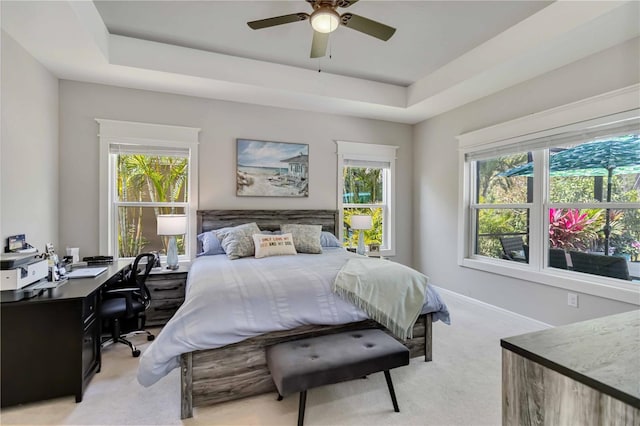 bedroom with light colored carpet, an office area, multiple windows, and a tray ceiling