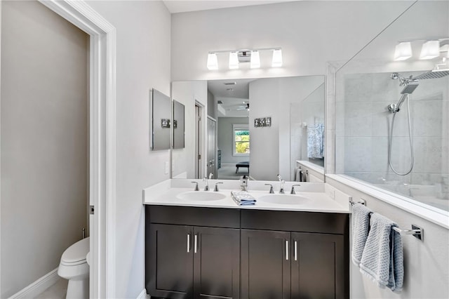 full bathroom featuring tiled shower, toilet, double vanity, and baseboards
