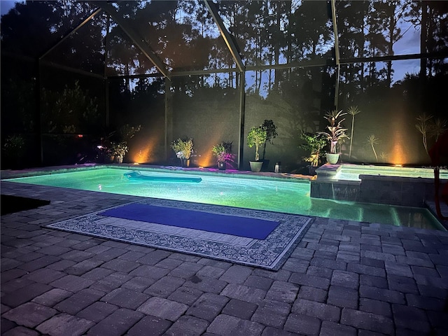 pool at twilight featuring glass enclosure, a patio, and a pool with connected hot tub