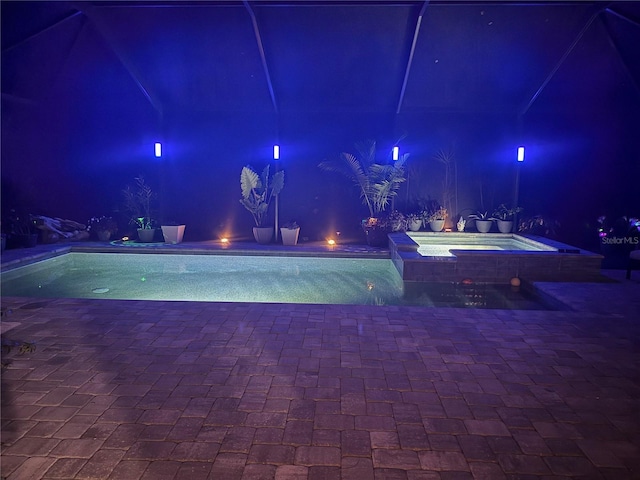 pool at night with an in-ground hot tub, an outdoor pool, and a patio area