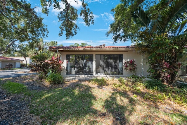 back of property featuring stucco siding, a sunroom, and a tile roof