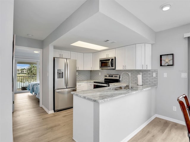 21687/689 Indian Bayou Dr, Fort Myers Beach, FL 33931 - kitchen featuring white cabinets, a peninsula, stainless steel appliances, a sink, and light wood-type flooring
