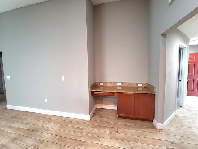 interior space with baseboards, built in study area, brown cabinets, and light stone counters