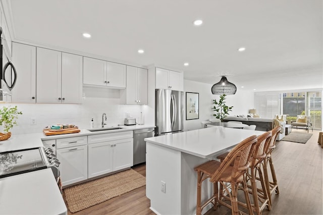 kitchen featuring stainless steel appliances, a sink, a kitchen island, white cabinetry, and light wood-type flooring