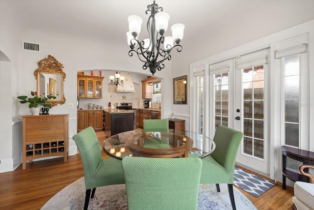 dining space with visible vents, wood finished floors, arched walkways, a wealth of natural light, and an inviting chandelier