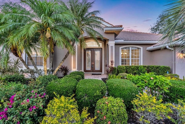 doorway to property featuring french doors, a tile roof, and stucco siding