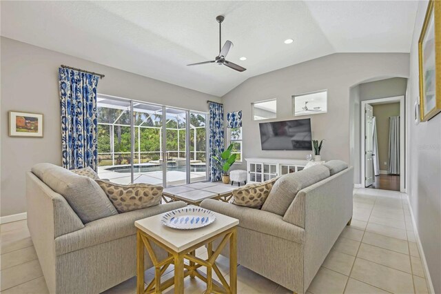 living area with baseboards, a sunroom, arched walkways, a ceiling fan, and vaulted ceiling
