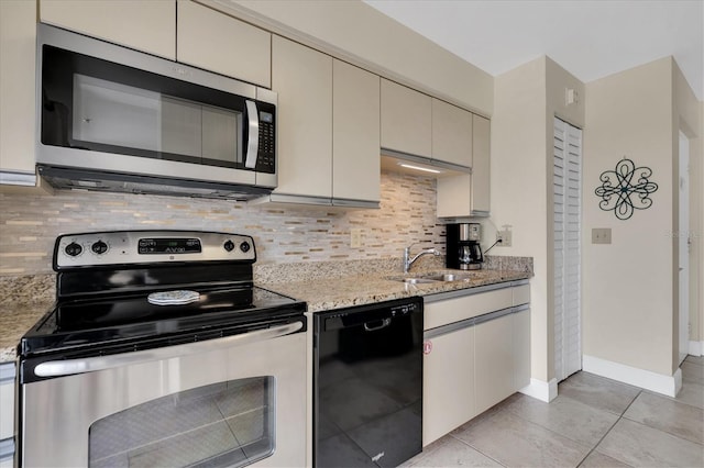 kitchen featuring cream cabinetry, tasteful backsplash, light stone counters, a sink, and stainless steel appliances
