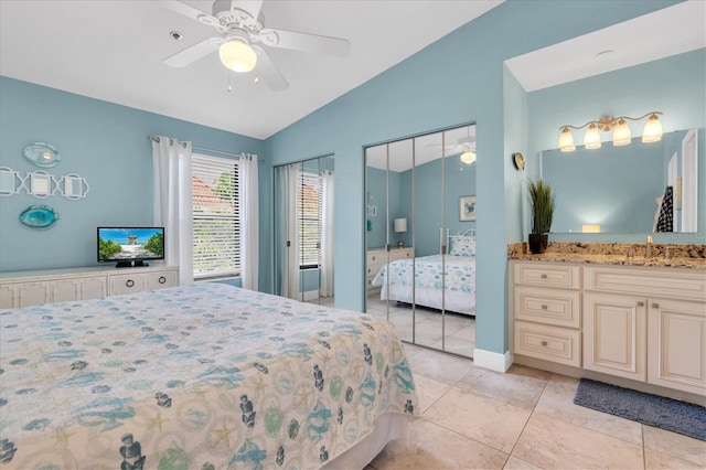 bedroom featuring multiple closets, light tile patterned flooring, ceiling fan, a sink, and vaulted ceiling