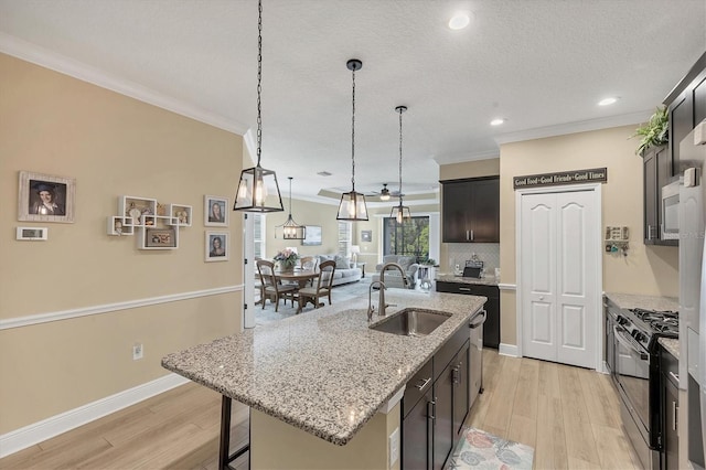 2628 Sapphire Blue Ln, Bradenton, FL 34211 - kitchen featuring gas stove, a sink, light wood-style flooring, crown molding, and an island with sink