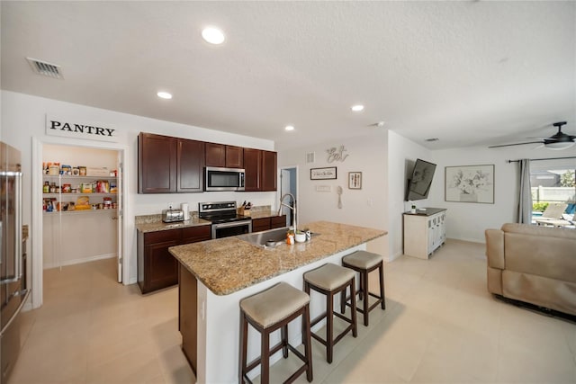 kitchen featuring a sink, a kitchen bar, open floor plan, stainless steel appliances, and a kitchen island with sink