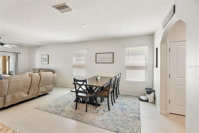 dining space with light tile patterned flooring, a textured ceiling, visible vents, ceiling fan, and arched walkways