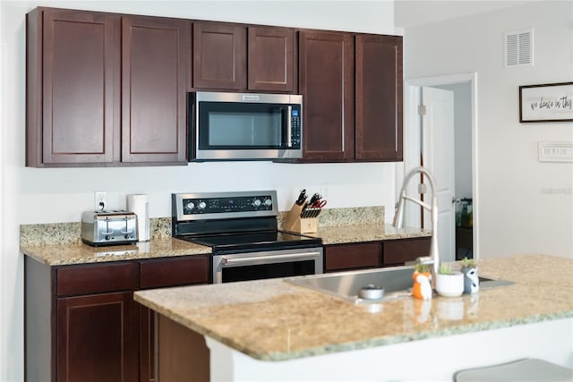 kitchen with light stone counters, dark brown cabinetry, a sink, appliances with stainless steel finishes, and visible vents