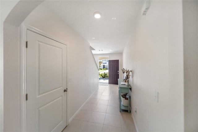 hall featuring light tile patterned flooring, baseboards, and arched walkways