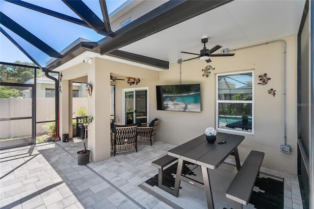 view of patio featuring glass enclosure, fence, and a ceiling fan