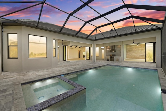 9241 Starry Night Ave, Sarasota, FL 34241 - pool at dusk with glass enclosure, a pool with connected hot tub, a patio area, exterior kitchen, and ceiling fan