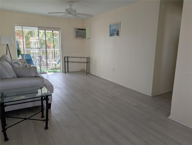 living room with a wall mounted AC, wood finished floors, baseboards, and a ceiling fan