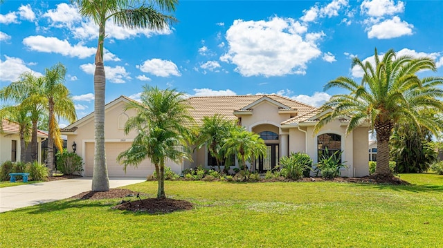 mediterranean / spanish-style home featuring a tile roof, stucco siding, driveway, a front yard, and a garage