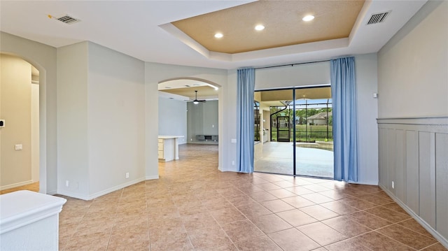 spare room featuring a tray ceiling, visible vents, arched walkways, and a ceiling fan
