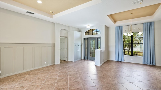 spare room with a tray ceiling, visible vents, a notable chandelier, and light tile patterned flooring