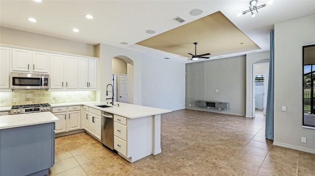 kitchen with a sink, a raised ceiling, stainless steel appliances, visible vents, and arched walkways