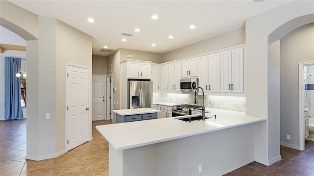 kitchen featuring visible vents, a kitchen island, tasteful backsplash, arched walkways, and appliances with stainless steel finishes